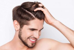 Stock image of a male model holding hair with left hand smiling and feeling confident